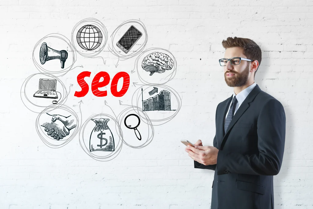 A man in a suit stands holding a smartphone, gazing at a wall with the word "SEO" in red, surrounded by icons symbolizing various concepts. mintdigitalsolutions